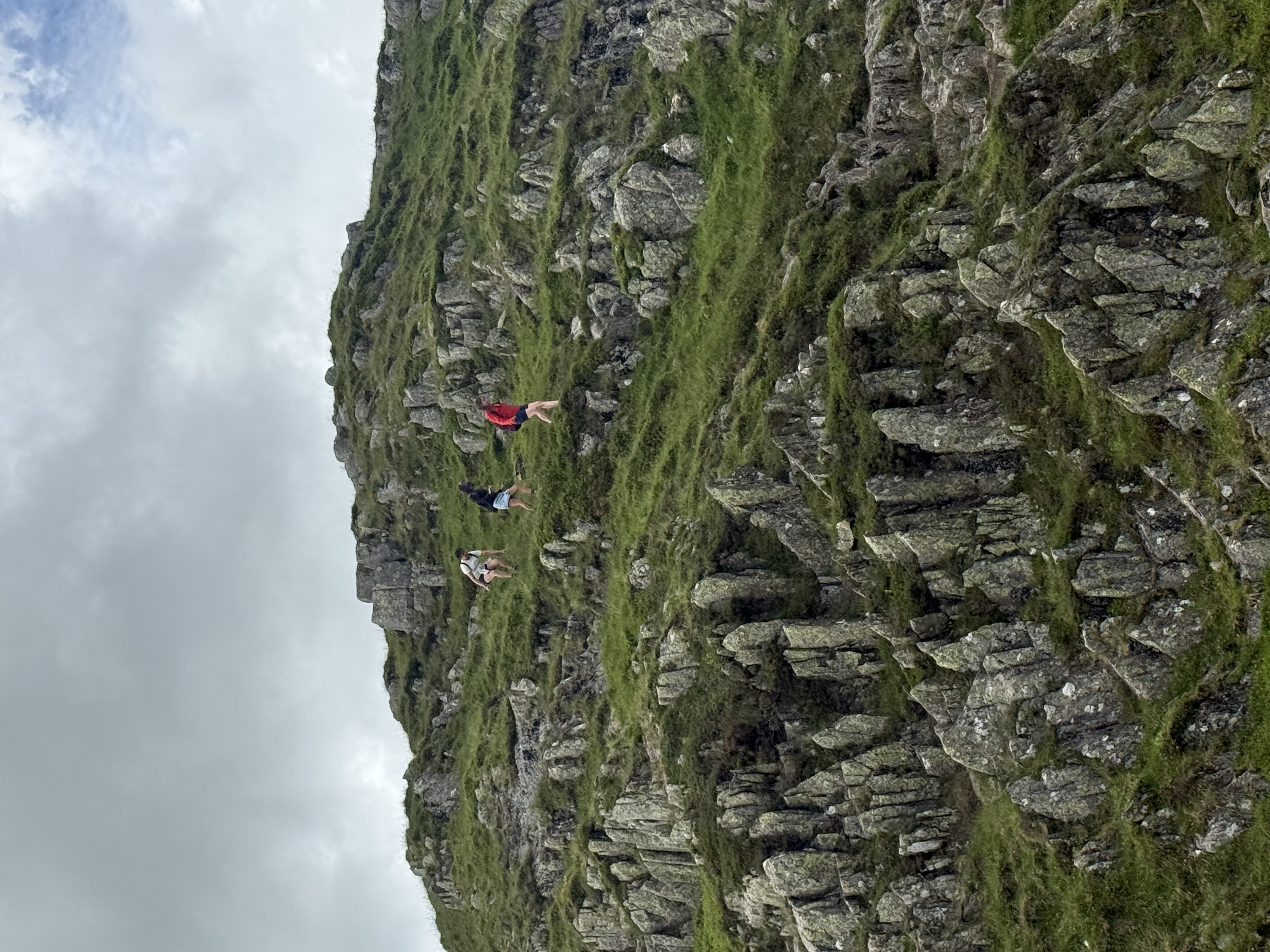 Three hikers scrambling up a steep rocky, grassy fellside