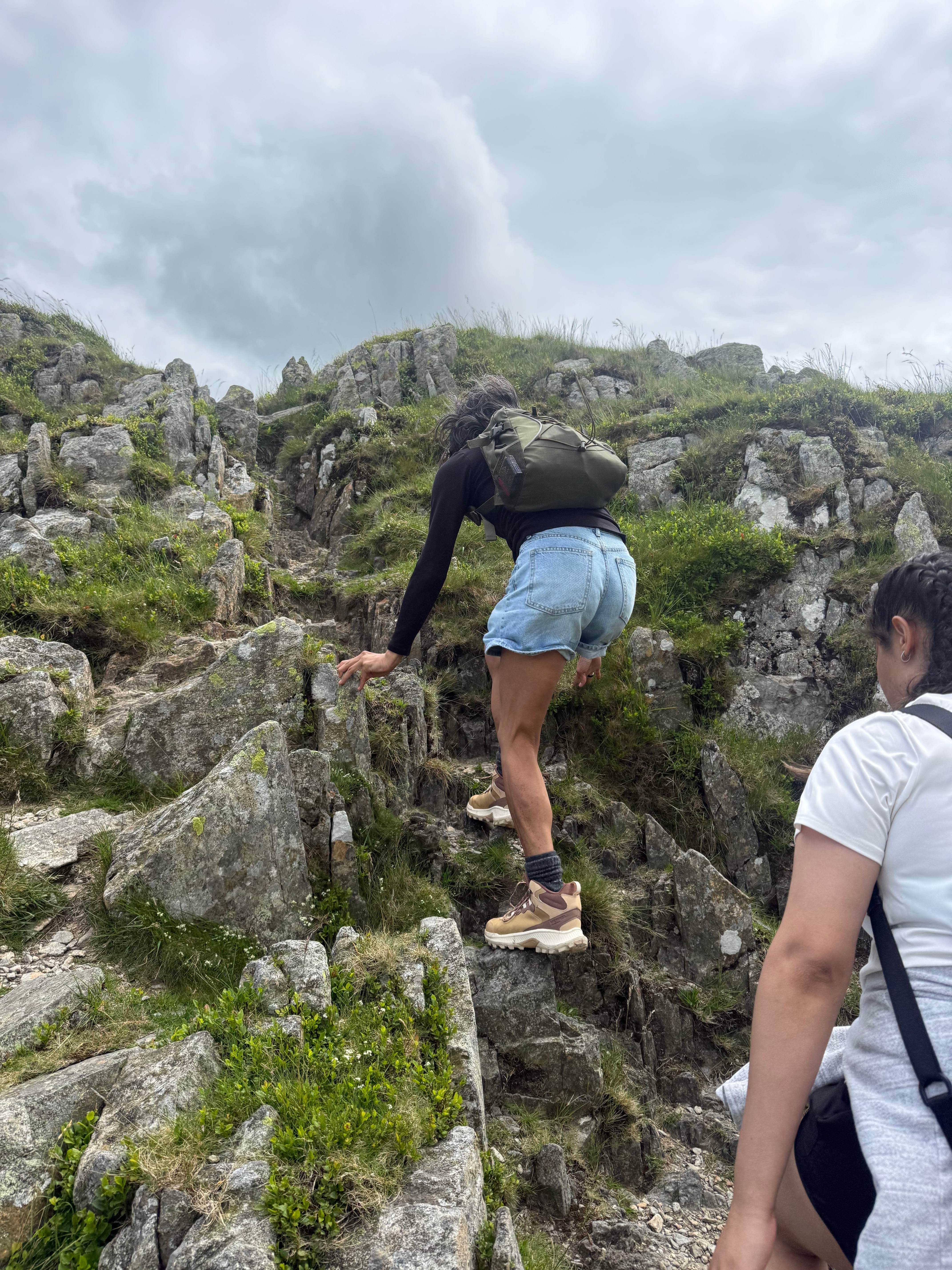 Woman scrambling up a rocky outcrop with another following close behind