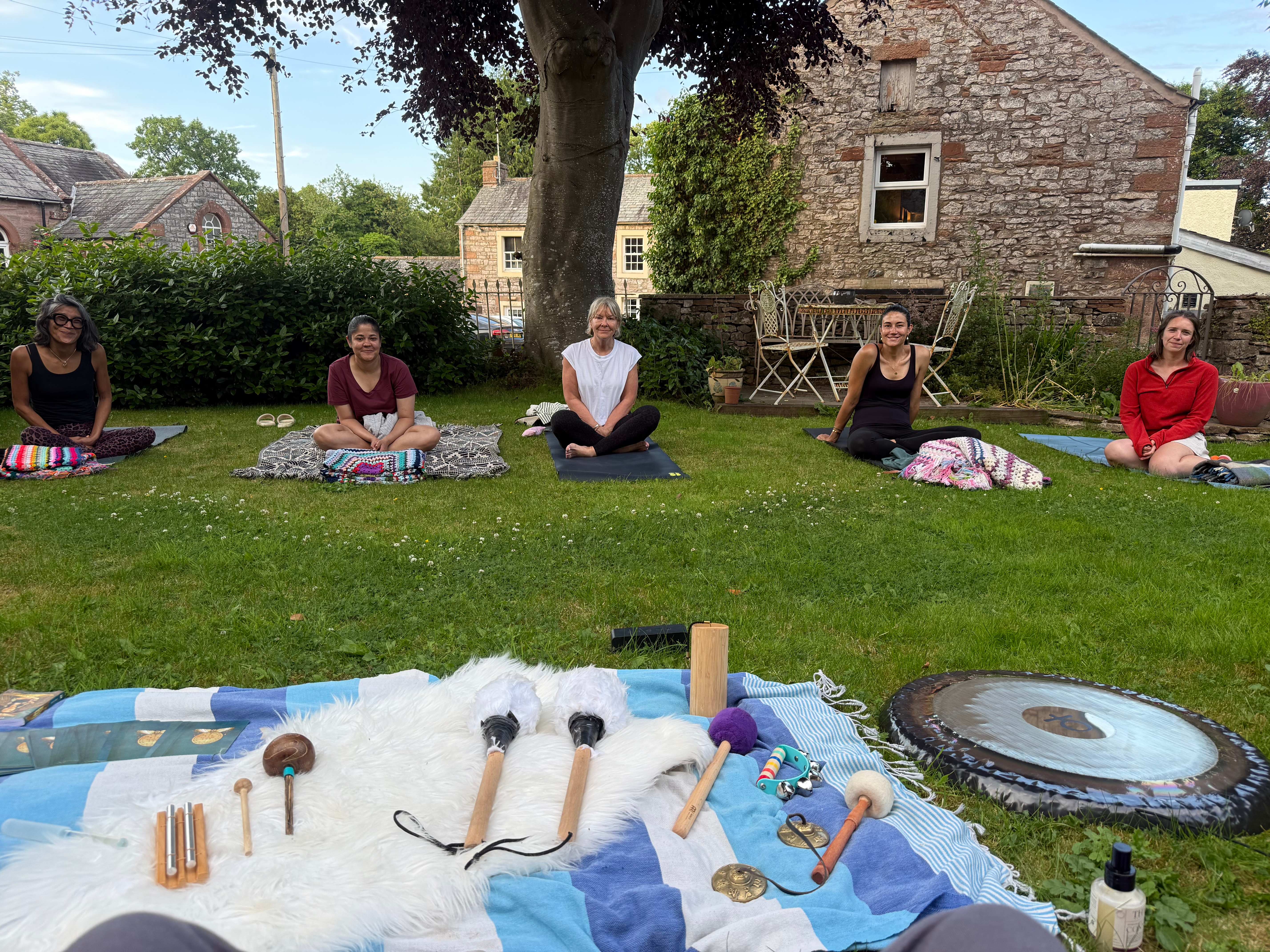Women sitting cross-legged in the garden before an outdoor sound bath