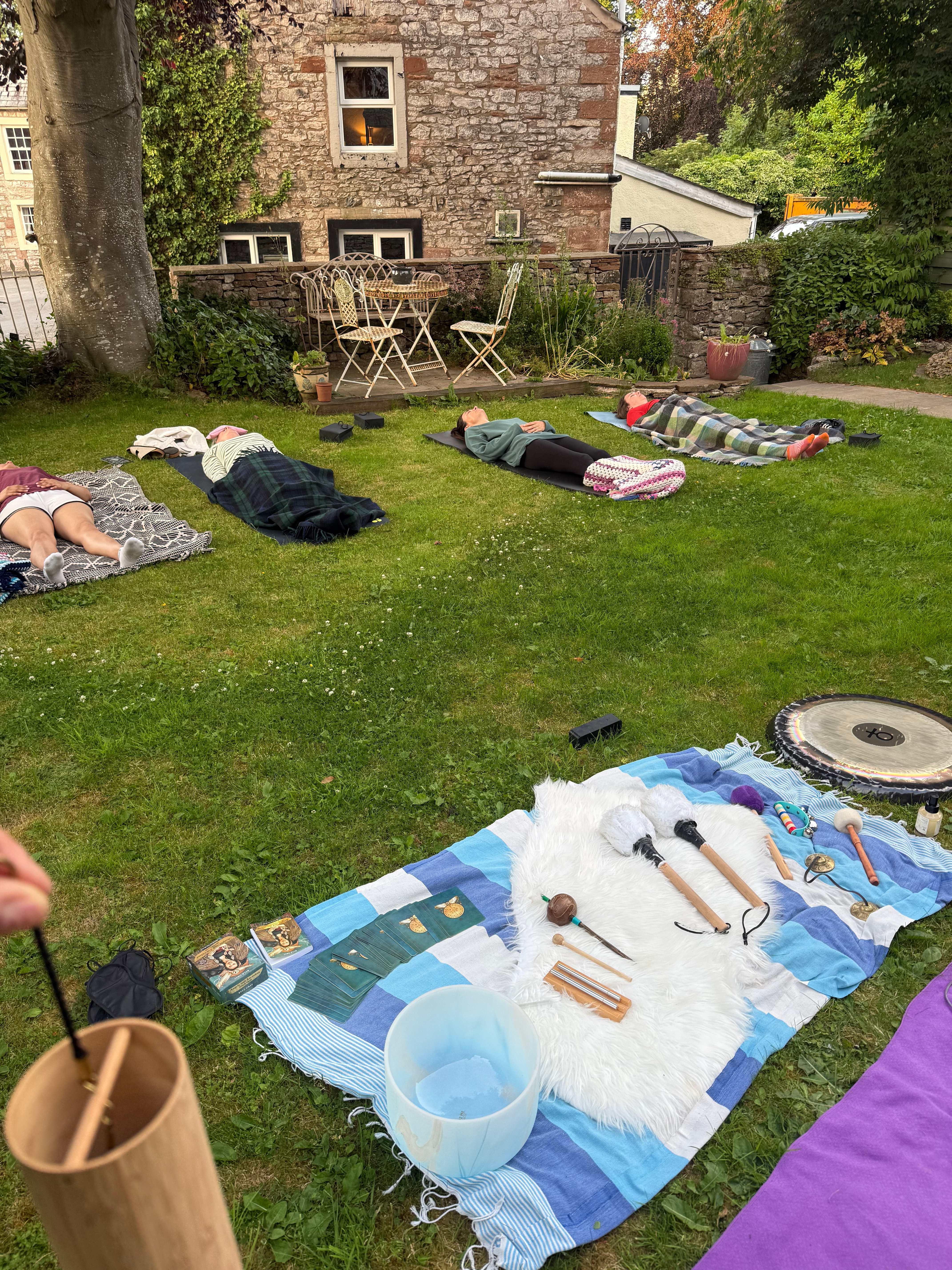 Women resting on mats and blankets on the lawn during an outdoor sound bath with gong and bowls