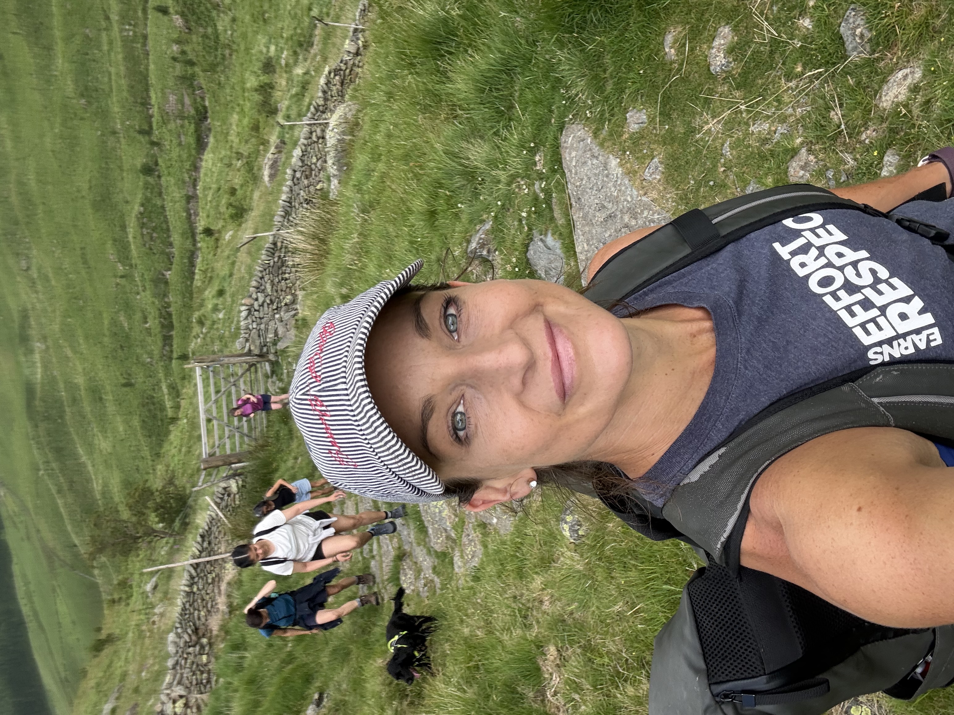 Close-up trail selfie of a woman in a striped cap with the group and spaniel climbing the stone path behind