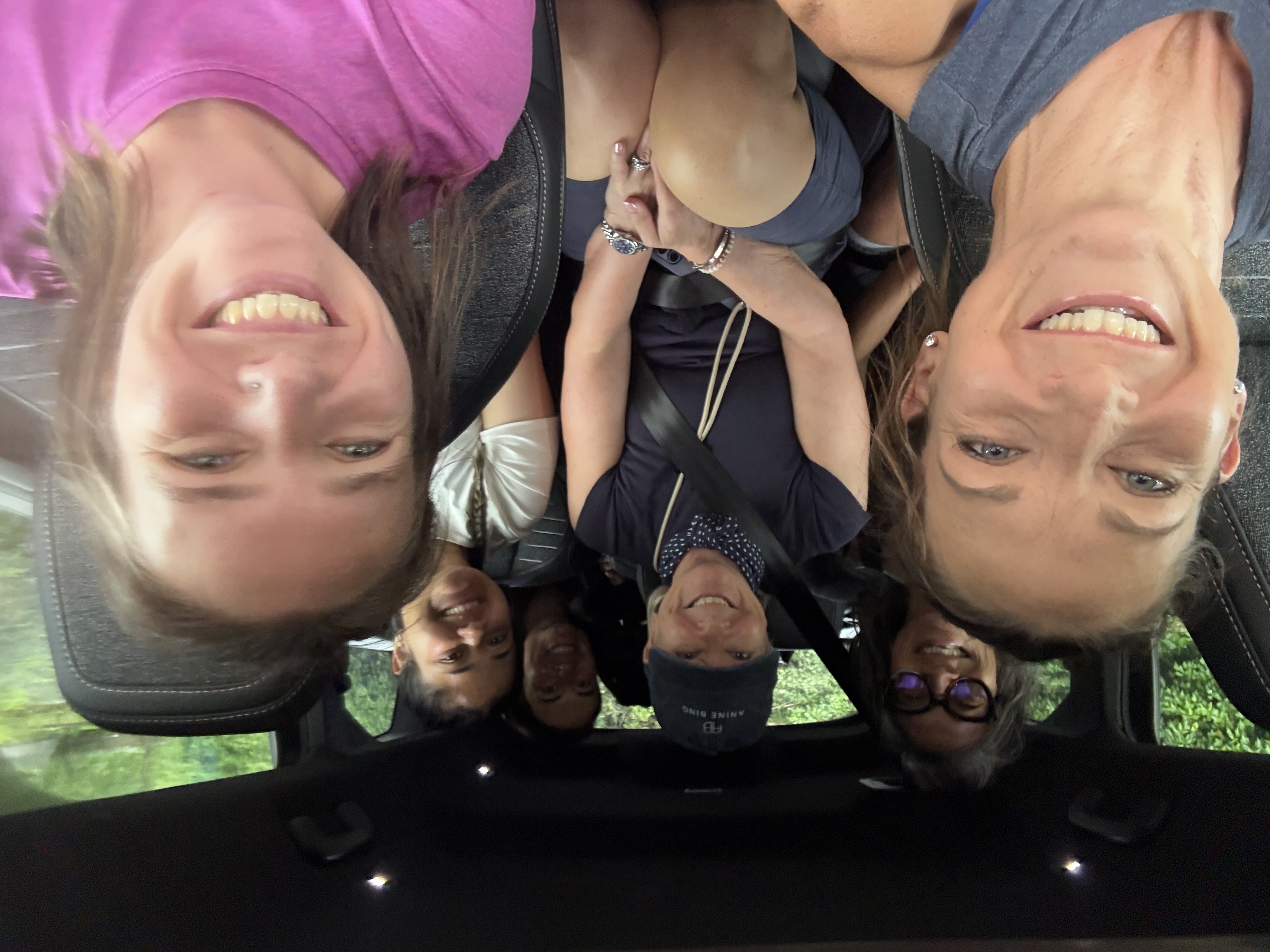 Group selfie of six smiling women packed into the van on the way to a hike