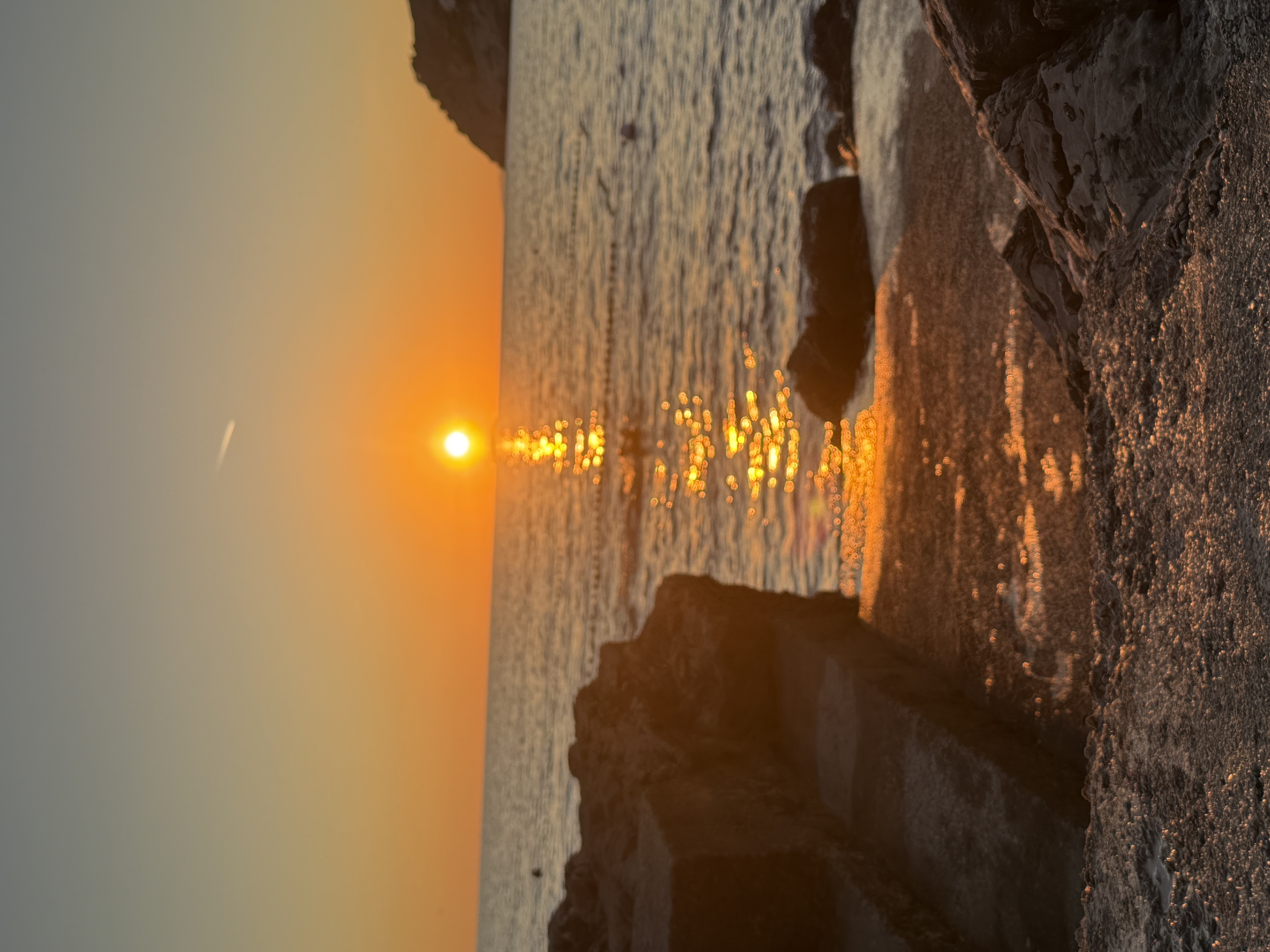 Golden sunset over the Adriatic Sea seen from a rocky shoreline, with sunlight glittering across the water