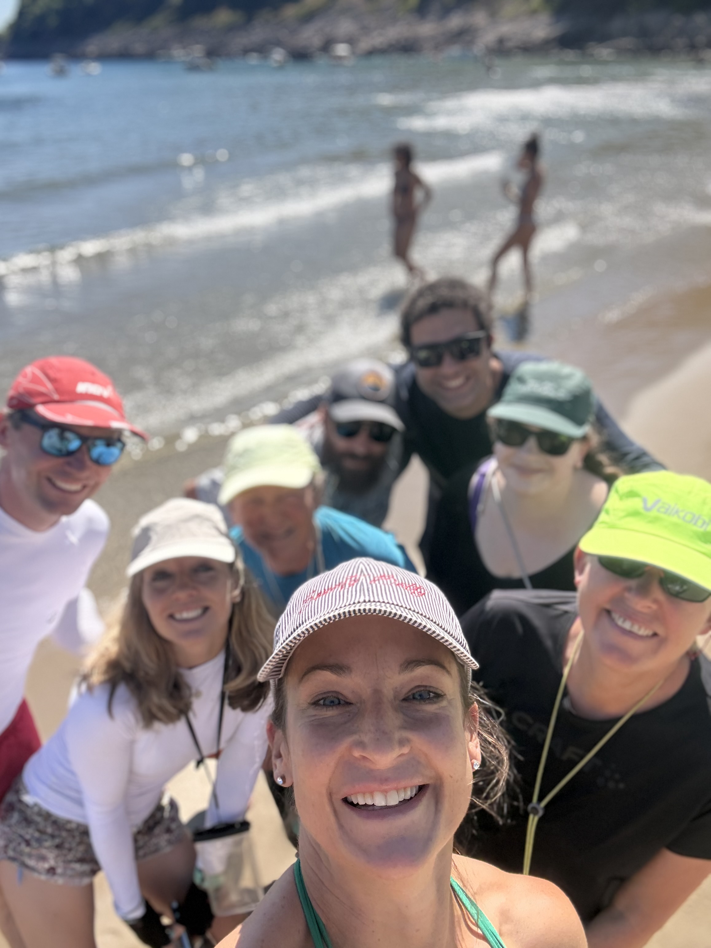 A group of smiling friends in caps taking a selfie on a sunny beach