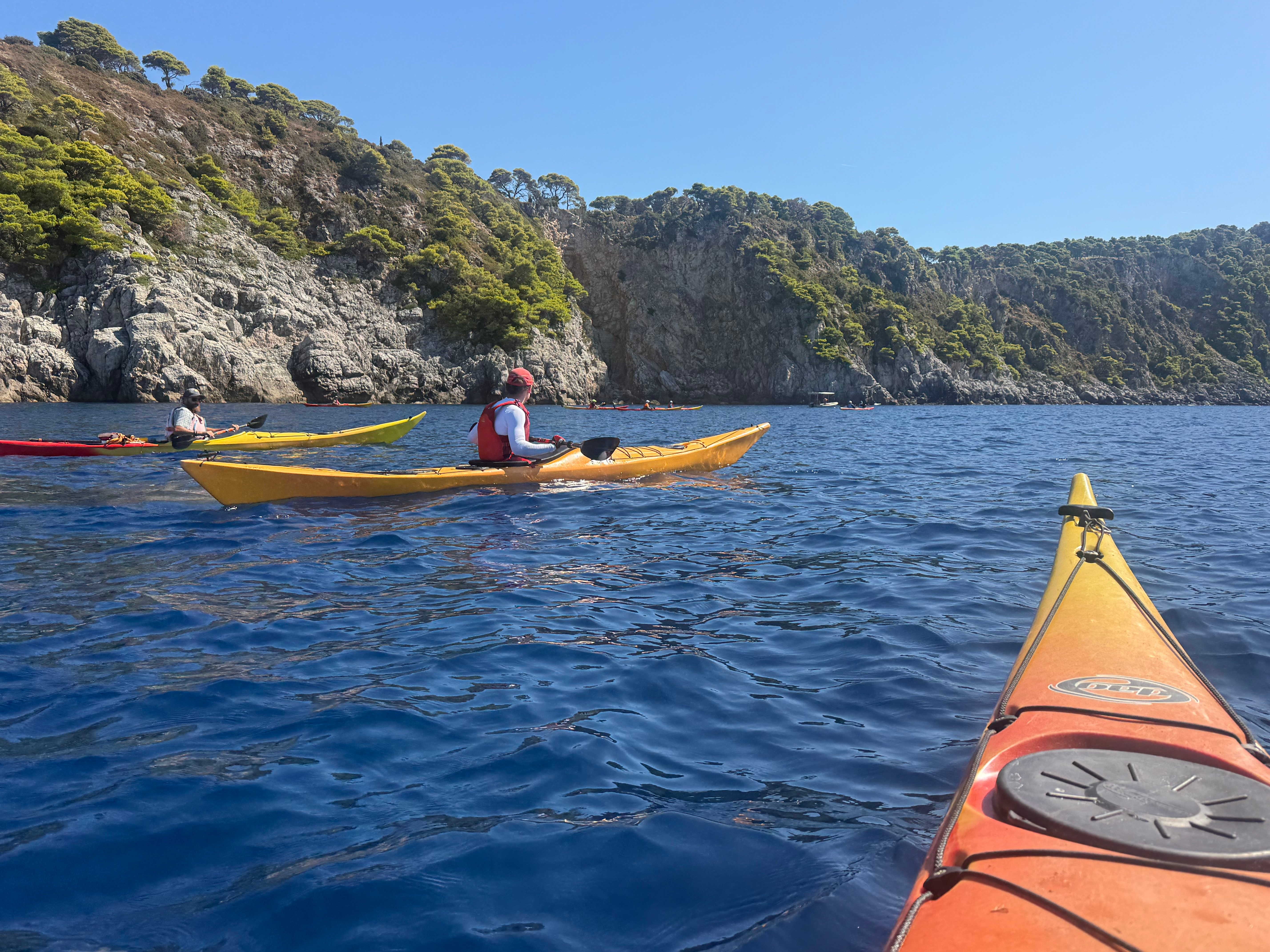 Kayakers paddling along steep pine-topped limestone cliffs on deep blue water